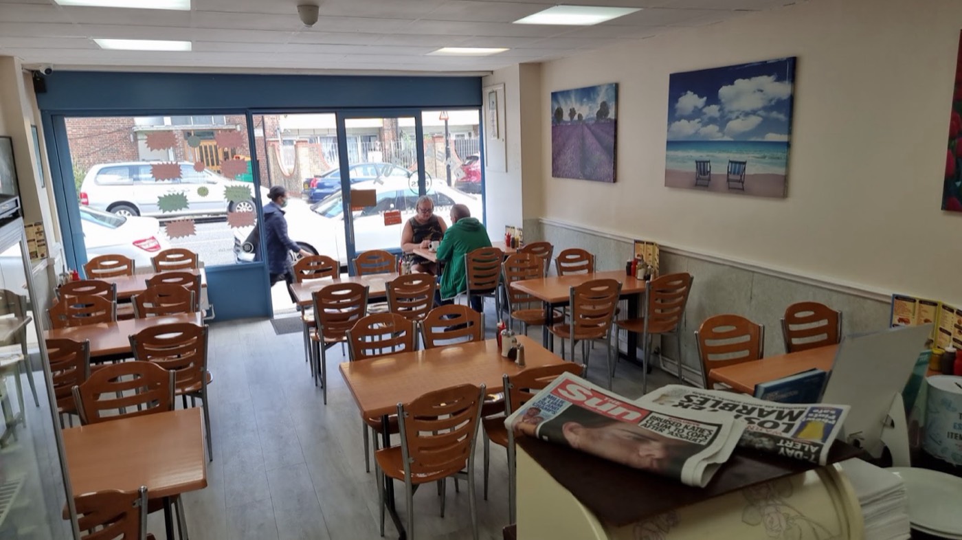 Inside Plaistow Cafe — bright dining room with wooden chairs, formica tables and the counter at the back